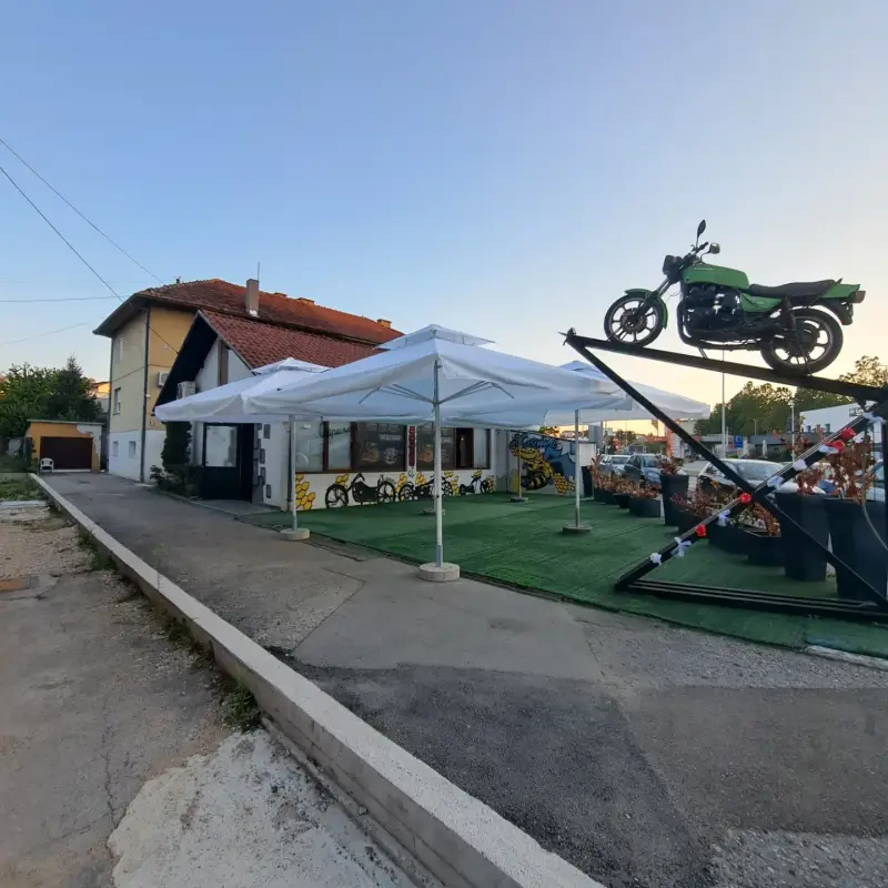 Bijeli suncobrani na terasi lokala, u prvom planu motocikl kao ukras
