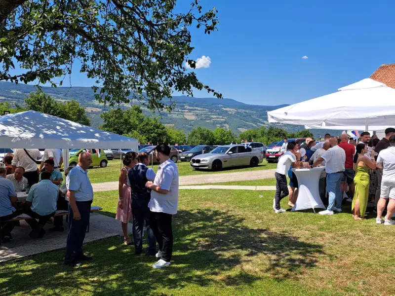 Svatovi na travnjaku ispred kuće, pored njih barski stolovi i suncobrani