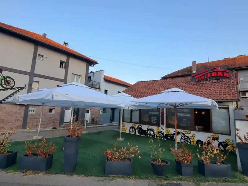 Bijeli suncobrani na terasi ispred lokala, uz cvijeće u žardinjerama